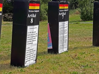 Skulpturenpark Drei große schwarze Säulen mit weißen Texttafeln über Artikel des Grundgesetzes in einem grünen Park.
