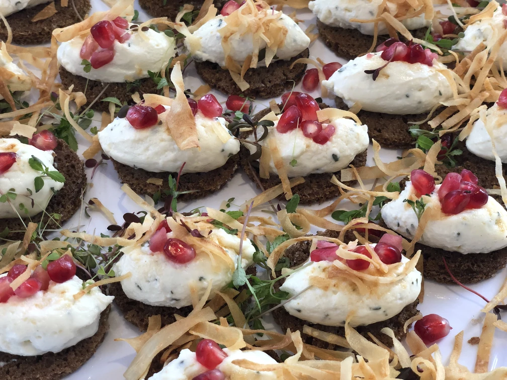 Kalte Platte  Eine Ansammlung von Roggenbrotscheiben, belegt mit cremigem Käse und garniert mit Granatapfelkernen.