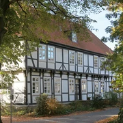 Herrenhaus Stift Quernheim Historisches Fachwerkhaus umgeben von Bäumen, mit rotem Dach und weißen Fensterrahmen im Sonnenschein.