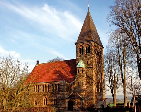 Backsteinkirche Hagedorn mit markantem Turm umgeben von kahlen Bäumen an einem sonnigen Tag.