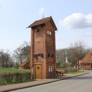 Backsteingebäude in ländlicher Umgebung, umgeben von Bäumen und angrenzend an eine ruhige Straße.