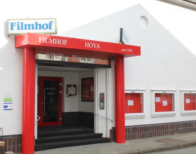 Filmhof Hoya mit roter Fassade und Markise, Kinotafeln, begehbarer Eingang.