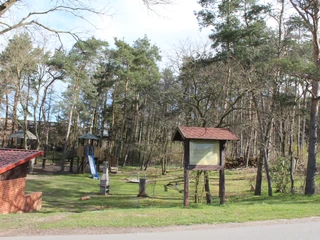 Grabhügelfeld Calle Ein Spielplatz mit Rutsche und Schaukeln, umgeben von hohen Bäumen und einer Holzhütte.