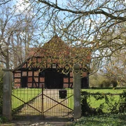 Behrenhof Fachwerkhaus mit Backsteinmauern hinter einem schmiedeeisernen Tor, umgeben von grüner Landschaft.