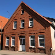 Ehem. Synagoge Rehburg Backsteingebäude mit weißen Fenstern, spitzem Dach und Eingang auf einer ruhigen Straße unter blauem Himmel.