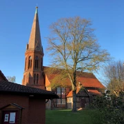 Kirche Estorf Die Kirche in Estorf, ein roter Backsteinbau mit hohem Turm, umgeben von Bäumen im Sonnenlicht.