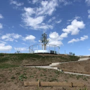 Aussichtsplattform Leese Eine runde Aussichtsplattform mit Geländer und Baum in zentraler Position vor blauem Himmel mit Wolken.