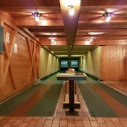 Farchanter Kegelkeller Zwei Kegelbahnen nebeneinander im Kegelkeller Farchant . Vorne steht ein Tisch, links an der Wand ist eine Tafel befestigt und an der Decke befinden sich Lampen