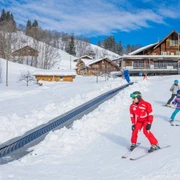 Skilehrer mit Kindern am Übungshang mit Förderband bei bestem Winterwetter