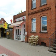 Eiscafé Picolo Eine rote Backsteinfassade mit Vordach, daneben Stühle; liegt an einer gepflasterten Straße.