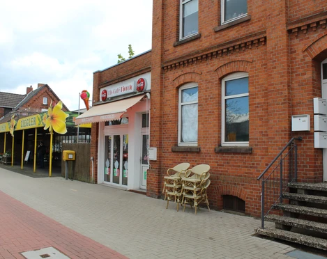 Eiscafé Picolo Eine rote Backsteinfassade mit Vordach, daneben Stühle; liegt an einer gepflasterten Straße.