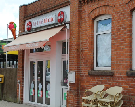 Eingang des Eiscafés Picolo mit roten Backsteinen und einem Sonnen-Markise an der Fassade.