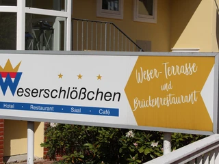 Brückenrestaurant Schild des Weserschlößchens mit Verweis auf Hotel, Restaurant und Brückenrestaurant auf gelbem Hintergrund.