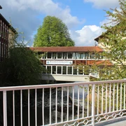 Brückenrestaurant Ein Restaurant auf einer Fußgängerbrücke verbindet zwei Gebäude über einem Fluss in üppiger Natur.