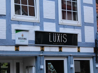 Luxis Meatbar in einem weißen Fachwerkhaus mit grauen Akzenten und einem Veltins Schild.