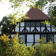 Alte Oberförsterei Uchte Altes Fachwerkgebäude mit rotem Ziegeldach, umgeben von Bäumen, künstlerisch eingefangen.