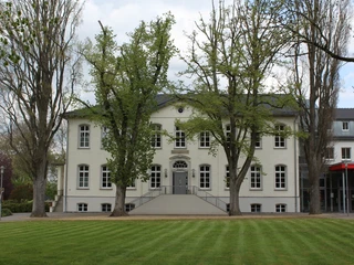 Besselscher Hof Historisches zweistöckiges Gebäude mit heller Fassade, umgeben von Bäumen und gepflegtem Rasen.