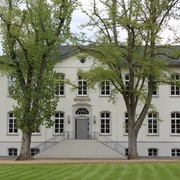 Besselsche Hof Ein weißes, zweistöckiges Gebäude mit symmetrischen Fenstern, umgeben von grünen Bäumen und Rasenflächen.