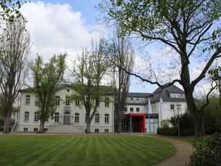 Besselscher Hof Der Besselsche Hof ist ein elegantes weißes Herrenhaus mit roten Akzenten, umgeben von Bäumen.