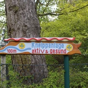 Kneippanlage Hoya Wegweiser zur Kneippanlage, umgeben von Bäumen und Pflanzen, weist in 100 Metern auf das Ziel hin.