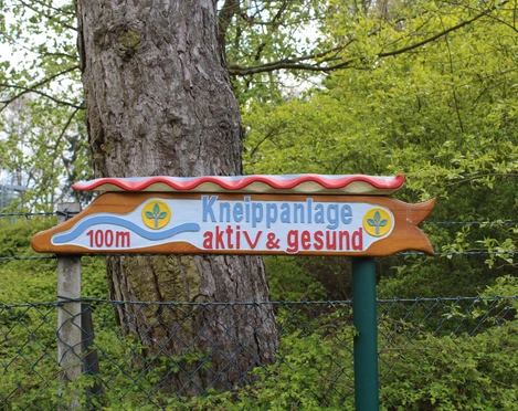 Kneippanlage Hoya Wegweiser zur Kneippanlage, umgeben von Bäumen und Pflanzen, weist in 100 Metern auf das Ziel hin.