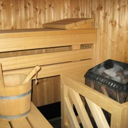 Sauna Holzverkleidete Sauna mit Holzbank, einer Kelle im Eimer und einem Ofen voller Sauna-Steine.