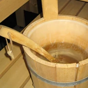 Sauna (3)bearb.jpg Ein hölzerner Saunakübel mit Wasser steht auf einer Holzbank neben einer Saunaaufguss-Kelle.