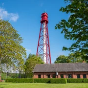 Campener Leuchtturm Blick auf den rot-weißen Campener Leuchtturm, im Bild Bäume, Deich und blauer Himmel