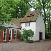 Historische Kapelle inmitten grüner Bäume. Ziegelbau mit Satteldach und einladendem Vorgarten.