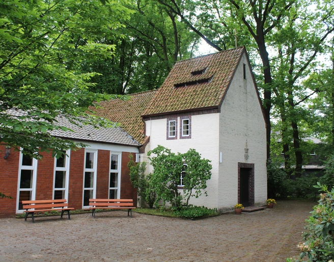 Historische Kapelle inmitten grüner Bäume. Ziegelbau mit Satteldach und einladendem Vorgarten.