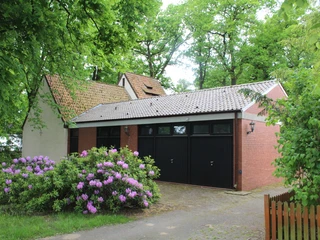 Kapelle in waldreicher Umgebung mit blühendem Rhododendron im Vordergrund und Backsteinfassade.