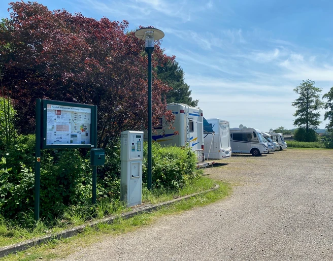 Wohnmobilstellplatz Rehburg Wohnmobilstellplatz mit mehreren Fahrzeugen neben grünen Büschen und einer Informationstafel unter blauem Himmel.
