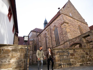Mittelalter-Atmosphäre auf Schloss Iburg Paar spaziert in Altstadtgasse, flankiert von historischen Steinhäusern und Kirche im Hintergrund.