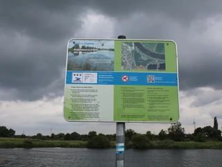 Alte Weser Ein Informationsschild in ländlicher Flusslandschaft unter bewölktem Himmel, nahe dem Wasser positioniert.