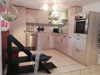 fewo-steinmann-kueche Moderne Einbauküche mit weißen Fronten, Elektrogeräten und beleuchtetem Deckenbereich auf hellen Fliesen.