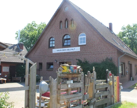 Haus der Vielfalt Backsteingebäude mit Satteldach und Schriftzug "Haus der Vielfalt", umgeben von Bäumen und Holzzaun.
