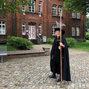 Nachtwächterin Martha van Acheim Nachtwächterin Martha van Acheim posiert mit Hellebarde vor einem historischen Backsteingebäude.