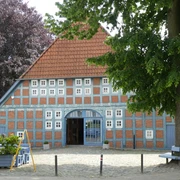 Historisches Fachwerkhaus mit blauen Fensterläden und rotem Ziegeldach unter grünen Bäumen.