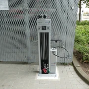 Lufttankstelle Bike & Ride Achimer Bahnhof Fahrrad-Luftstation am Achimer Bahnhof mit integrierter Pumpe, umgeben von Metallgitter und Pflanzen.