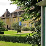 Gelbes Herrenhaus mit schiefergedecktem Dach und zahlreichen Fenstern, umgeben von gepflegtem Grün.