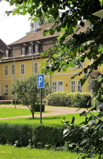 Gelbes Herrenhaus mit schiefergedecktem Dach und zahlreichen Fenstern, umgeben von gepflegtem Grün.