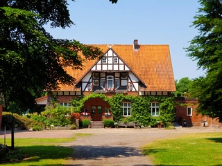 Haupthaus Lüttsche-Hoff Ein historisches Fachwerkhaus mit rotem Ziegeldach, umgeben von grüner Landschaft und einem gepflasterten Weg.