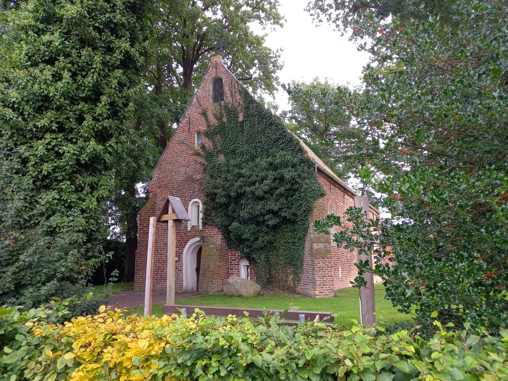 Kapelle Bokelesch Die kleine Kirche, idyllisch umgeben von üppigem Grün und Efeu, wirkt wie ein versteckter Schatz in der friedlichen Landschaft Niedersachsens. Der rote Backstein, teilweise von Pflanzen überwuchert, erzählt von Geschichten aus vergangenen Zeiten. Dies ist ein Ort der Stille, ideal für eine ruhige Einkehr oder um einfach nur die beruhigende Atmosphäre zu genießen. Der umliegende Garten lädt zu einem besinnlichen Spaziergang ein und bietet eine perfekte Kulisse für Momente der Besinnung und des Nachdenkens. Der Glockenturm erhebt sich dezent über die Bäume und verleiht dem kleinen Gebäude eine erhabene Anmut. Dies ist nicht nur ein Ort des Gebets, sondern auch ein Zeugnis der architektonischen Einfachheit und Schönheit vergangener Jahrhunderte. Ein Besuch dieser malerischen Kirche bietet sowohl kulturellen Reichtum als auch die Möglichkeit, die Schönheit der Umgebung zu genießen. Ob für stille Momente des Alleinseins oder um die Spiritualität des Ortes zu spüren, diese Kirche strahlt eine unvergessliche Ruhe und zeitlose Eleganz aus.