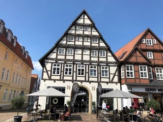 Patrizierhaus des Gödeke Schünemann Dreistöckiges Fachwerkhaus in Stadtkulisse, an beiden Seiten von Geschäften flankiert, blauer Himmel.
