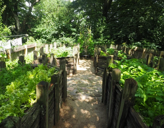 OLYMPUS DIGITAL CAMERA Steinerne Beeteinfassungen umrahmen eine Mischung aus grüner Vegetation und hellem Steinpfad.