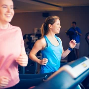 Zwei junge Frauen und ein Mann trainieren fröhlich auf Laufbändern in einem modernen Fitnessstudio.Two young women and a man are happily exercising on treadmills in a modern fitness studio.