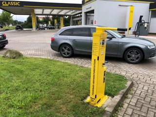 Lufttankstelle Hoya classic Eine gelbe Lufttankstelle steht auf einem Parkplatz vor einer Tankstelle mit mehreren Autos im Hintergrund.