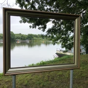 Weserblick 2021 Ein goldener Bilderrahmen steht am Weserufer, mit Blick auf den Fluss und die bewaldeten Uferbereiche.