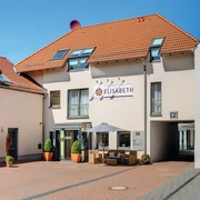 Außenansicht Hotel Elisabeth Hotel Elisabeth mit roten Ziegeldächern, begrünten Eingangspflanzen und Sitzbereich im Vordergrund.