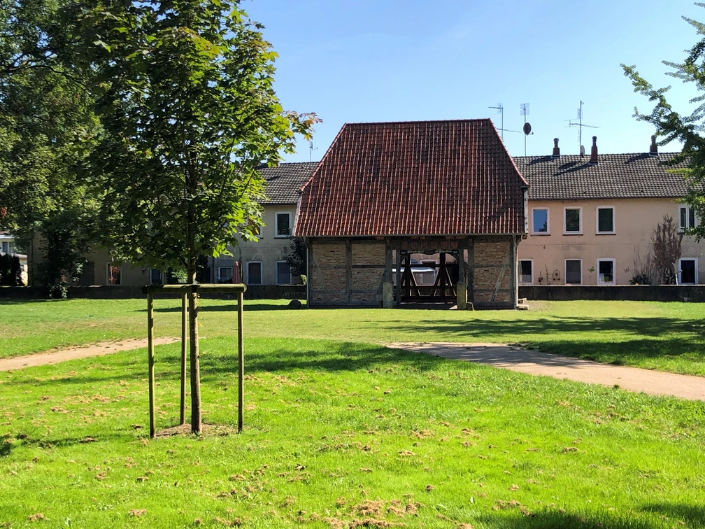 Ältestes Haus Hoya Backsteingebäude mit rotem Ziegeldach und hölzernen Stützen in einer grünen Parklandschaft.